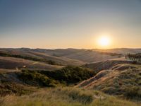 a sunset illuminates the landscape of an open plain with hills and green grass