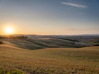 a sunset illuminates the landscape of an open plain with hills and green grass