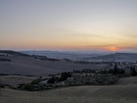 the sun is setting behind the hills in the country side of italy for people to admire