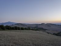 the sun is setting behind the hills in the country side of italy for people to admire