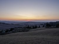 the sun is setting behind the hills in the country side of italy for people to admire