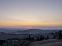 the sun is setting behind the hills in the country side of italy for people to admire