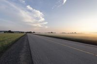 a wide paved road in an empty, rural area at sunset with a sky background