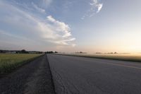 a wide paved road in an empty, rural area at sunset with a sky background