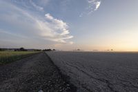 a wide paved road in an empty, rural area at sunset with a sky background