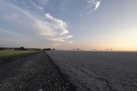 a wide paved road in an empty, rural area at sunset with a sky background