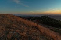 there is a sunset in the horizon on a field with grassy land below the mountains