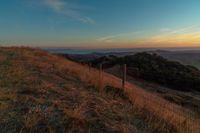 there is a sunset in the horizon on a field with grassy land below the mountains