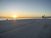 a lone man walking a dog across a sidewalk by the ocean at sunset with a colorful sky