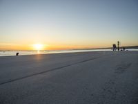 a lone man walking a dog across a sidewalk by the ocean at sunset with a colorful sky