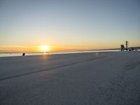 a lone man walking a dog across a sidewalk by the ocean at sunset with a colorful sky