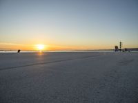 a lone man walking a dog across a sidewalk by the ocean at sunset with a colorful sky