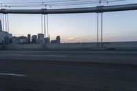 a long bridge with buildings in the background at sunset / taken from an suv on highway