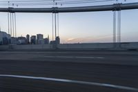 a long bridge with buildings in the background at sunset / taken from an suv on highway