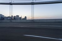 a long bridge with buildings in the background at sunset / taken from an suv on highway