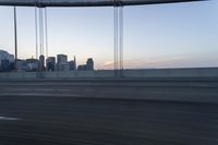 a long bridge with buildings in the background at sunset / taken from an suv on highway