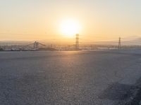 the sun sets behind power lines and power pylons over a town, on the horizon of a highway in this view