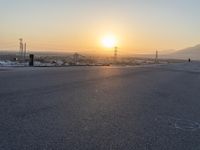 the sun sets behind power lines and power pylons over a town, on the horizon of a highway in this view