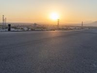 the sun sets behind power lines and power pylons over a town, on the horizon of a highway in this view