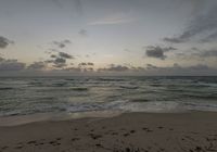 the ocean is moving rapidly towards the shore of a beach at sunset with dark clouds