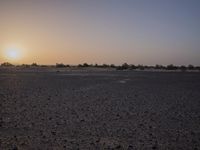 a desert area with sparse brown dirt and a sunset sky in the background behind it