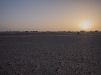 a desert area with sparse brown dirt and a sunset sky in the background behind it