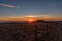 there is a sunset in the horizon on a field with grassy land below the mountains