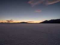 a picture of the sun setting over the mountains as seen from across a snowy plain