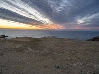 a view of the ocean with a large kite flying over it at sunset on top of a hill