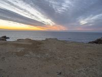 a view of the ocean with a large kite flying over it at sunset on top of a hill