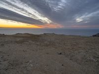 a view of the ocean with a large kite flying over it at sunset on top of a hill