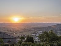 the sun is setting behind an orange orange sky above a city and hills in the background