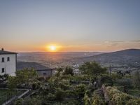 the sun is setting behind an orange orange sky above a city and hills in the background