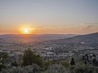 the sun is setting behind an orange orange sky above a city and hills in the background