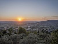 the sun is setting behind an orange orange sky above a city and hills in the background