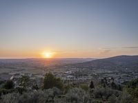 the sun is setting behind an orange orange sky above a city and hills in the background