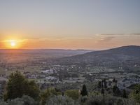 the sun is setting behind an orange orange sky above a city and hills in the background