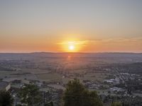 the sun is setting behind an orange orange sky above a city and hills in the background