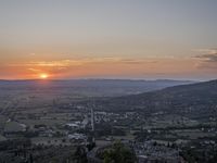 the sun is setting behind an orange orange sky above a city and hills in the background