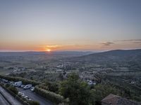 the sun is setting behind an orange orange sky above a city and hills in the background