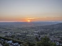 the sun is setting behind an orange orange sky above a city and hills in the background