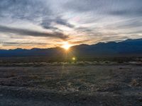 a photo of a sunset over some mountains and water with the sun in the middle of the day