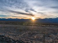 a photo of a sunset over some mountains and water with the sun in the middle of the day