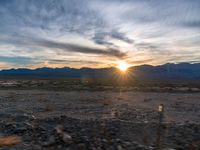 a photo of a sunset over some mountains and water with the sun in the middle of the day