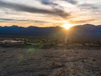 a photo of a sunset over some mountains and water with the sun in the middle of the day