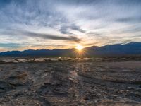 a photo of a sunset over some mountains and water with the sun in the middle of the day