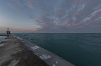 sunsets on the ocean over a pier and a blue ocean and pink clouds in the distance