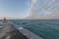 sunsets on the ocean over a pier and a blue ocean and pink clouds in the distance