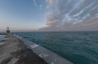 sunsets on the ocean over a pier and a blue ocean and pink clouds in the distance