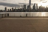 a person on the boardwalk near a fence overlooking a river and city skyline at sunset